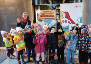Dzieci z nauczycielką w holu teatru przed plakatem przedstawienia