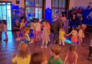 dzieci tańczą i bawią przy zasłoniętych oknach, aby widać było neonowe bransoletki i inne ozdoby fluorescencyjne