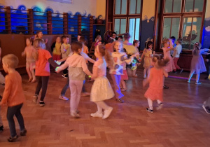 dzieci tańczą i bawią przy zasłoniętych oknach, aby widać było neonowe bransoletki i inne ozdoby fluorescencyjne