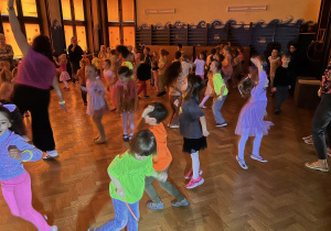dzieci tańczą i bawią przy zasłoniętych oknach, aby widać było neonowe bransoletki i inne ozdoby fluorescencyjne