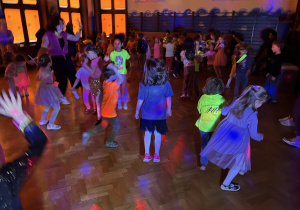 dzieci tańczą i bawią przy zasłoniętych oknach, aby widać było neonowe bransoletki i inne ozdoby fluorescencyjne