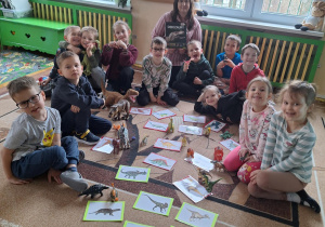 Na zdjęciu dzieci z Panią dopasowują figurki dinozaurów do zdjęć.