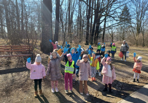 Grupa dzieci w parku pokazuje rączki zaopatrzone w niebieskie jednorazowe rękawiczki