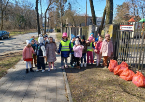 dzieci stoja przedwejsciem na teren przedszkola, obok płotu leżą worki z zebranymi śmieciami