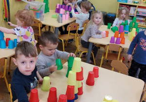dzieci siedzą przy stolikach – układają wieże z kolorowych kubeczków