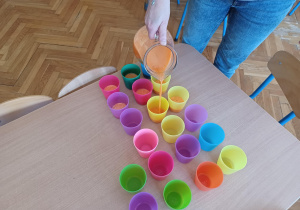 na stoliku stoją kolorowe kubeczki, do których n-lka nalewa przygotowany przez dzieci sok