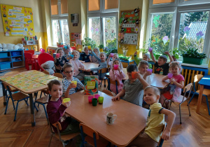 dzieci siedzą przy stolikavch i pija z kolorowych kubeczków przygotowany przez nie sok z marchewki i jabłek