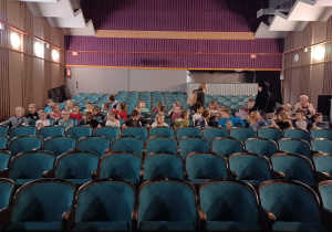 Grupa dzieci siedzi na krzesełkach na widowni teatru