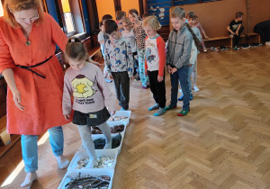 dzieci pokonujące leśną ścieżkę sensoryczną, obok dzieci prowadzącą zabawę