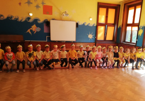 Zdjęcie przedstawia dzieci z grupy czwartej siedzące na ławce w żółtych koszulkach