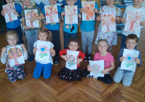 W dniu "kropki"grupa uśmiechniętych dzieci prezentuje w swojej klasie prace plastyczne wykonane farbami. Prace przedstawiają kolorowe drzewa i kwiaty.