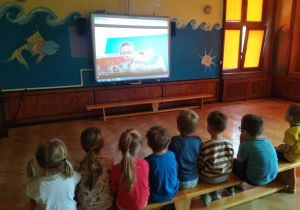 Tata Rodryka i Rodryk czytają bajkę dla kolegów z grupy pszczółek siedzących przed tablicą multimedialną