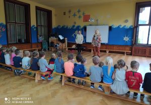 Przedszkolaki siedząc na ławce słuchają koncertu muzycznego w wykonaniu naszych gości