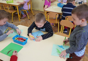 Zdjęcie przedstawia dzieci ozdabiające papierowe wiatraczki.