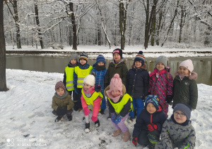 Dzieci z grupy pszczółek pozują do zdjęcia na tle zimowego krajobrazu