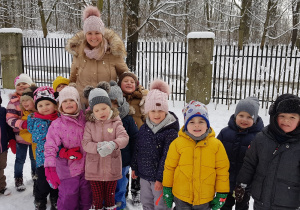 Zdjęcie przedstawia całą grupę wraz z nauczycielką w przedszkolnym ogródku.