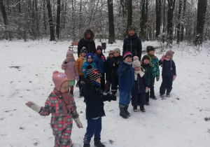Na zdjęciu widać dzieci oraz panie z grupy na spacerze w parku. W tle drzewa i śnieg.