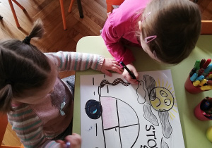 Na zdjęciu widać dwoje dzieci siedzących przy stoliku i robiących plakat.