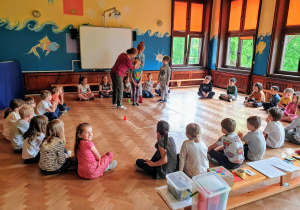 Dzieci siedzą w kręgu podczas zabawy- Idź według wskazówek.