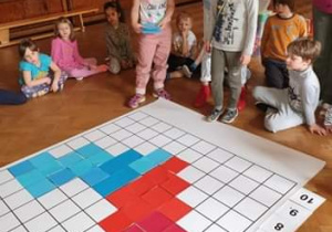 Dzieci układają na macie do kodowania serce z czerwonych i niebieskich kwadratów dla mamy i taty.