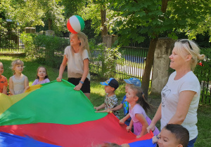 Na zdjęciu dzieci bawiące się razem z nauczycielkami chustą animacyjną.