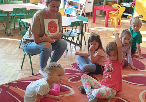 Na zdjęciu dzieci siedzące na dywanie, rozmawiające z nauczycielką o książce "Kropka".