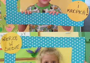 Na zdjęciu dwoje dzieci pozujących w niebieskiej ramce w kropki z napisem :Wierzę w siebie.. i kropka!"