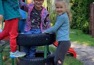 Na zdjęciu uśmiechnięta grupa dzieci na urządzeniu na placu zabaw.