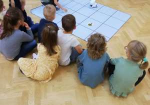 Dzieci siedzą przed mata do kodowania, na macie chłopiec układa obrazki