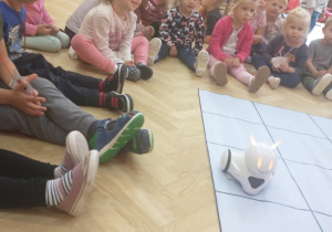 Na zdjęciu dzieci przyglądające się działaniu robota na specjalnej macie