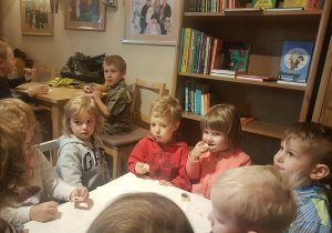 dzieci siedzą przy stolikach, jedzą ciasteczka