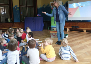 Prowadząca stoi przed dziećmi, rozkłada ręce