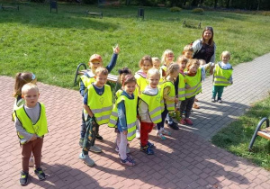 zdjęcie przedstawia dzieci wraz z nauczycielką podczas spaceru po parku.
