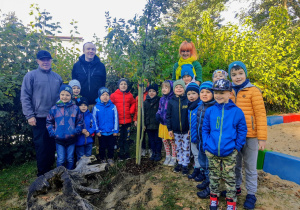 Dzieci z grupy szóstej "Słoneczka" wraz z nauczycielką, Panem Piotrem oraz Panem Maciejem pozują na tle zasadzonego grupowego drzewa