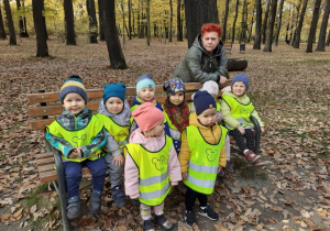 Zdjęcie przedstawia dzieci siedzące na ławeczce w parku