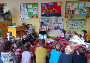 na zdjęciu dzieci z grupy III i V oglądające plakat z numerem alarmowym prezentowany przez nauczyciela
