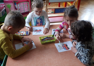 na zdjęciu dzieci z grupy III i V oglądające plakat z numerem alarmowym prezentowany przez nauczyciela