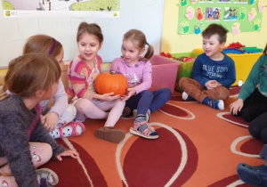 Na zdjęciu dzieci siedzą w kole i podają sobie dynie.