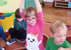 Na zdjęciu dziewczynka podnosząca dynię wysoko nad głowę.