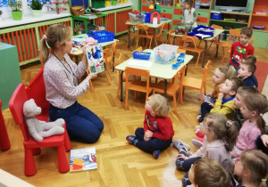 dzieci siedząć na dywanie, słuchają nauczycielki czytającej książkę o misiach