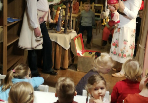 dzieci oglądają spektakl " Jasełka w "Baśniowej Kawiarence" - w tle aktorzy z lalkami