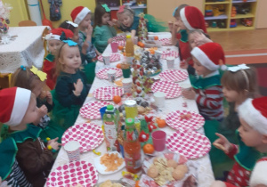 Zdjęcie przedstawia dzieci siedzące przy stole z przysmakami.