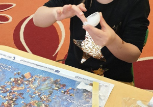 Na zdjęciu dziewczynka smarująca plastikową bombkę klejem.