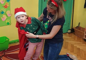 Na zdjęciu chłopiec losujący prezent z czerwonego worka trzymanego przez nauczycielkę.