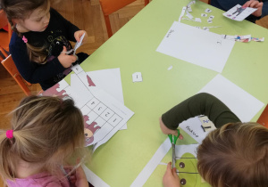 Dzieci przy stolikach wycinają puzzle i naklejają w odpowiednim ułożeniu na kartce