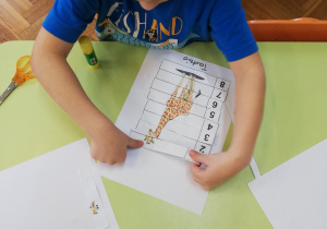 Dzieci przy stolikach wycinają puzzle i naklejają w odpowiednim ułożeniu na kartce