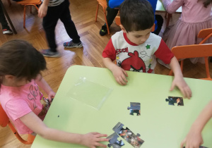 Dzieci przy stolikach w małych zespołach układają puzzle na czas​