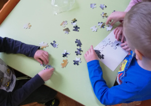 Dzieci przy stolikach w małych zespołach układają puzzle na czas​