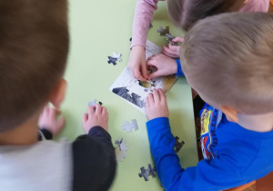 Dzieci przy stolikach w małych zespołach układają puzzle na czas​