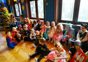 Pracownicy przedszkola i dzieci w przebraniach karnawałowych siedzą na ławkach.